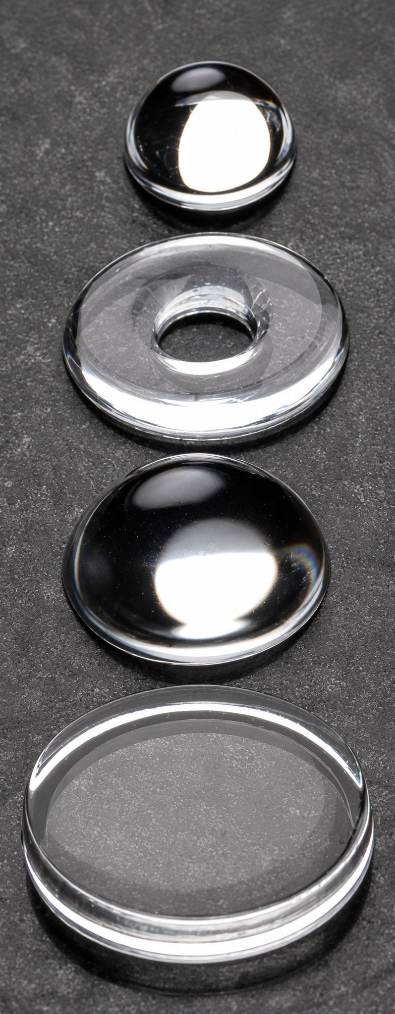 Four silicone optical components arranged vertically on a bench: dome lens, ring lens, plano-convex lens, and flat window