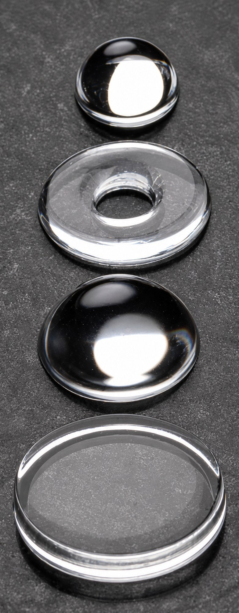 Four silicone optical components arranged vertically on a bench: dome lens, ring lens, plano-convex lens, and flat window